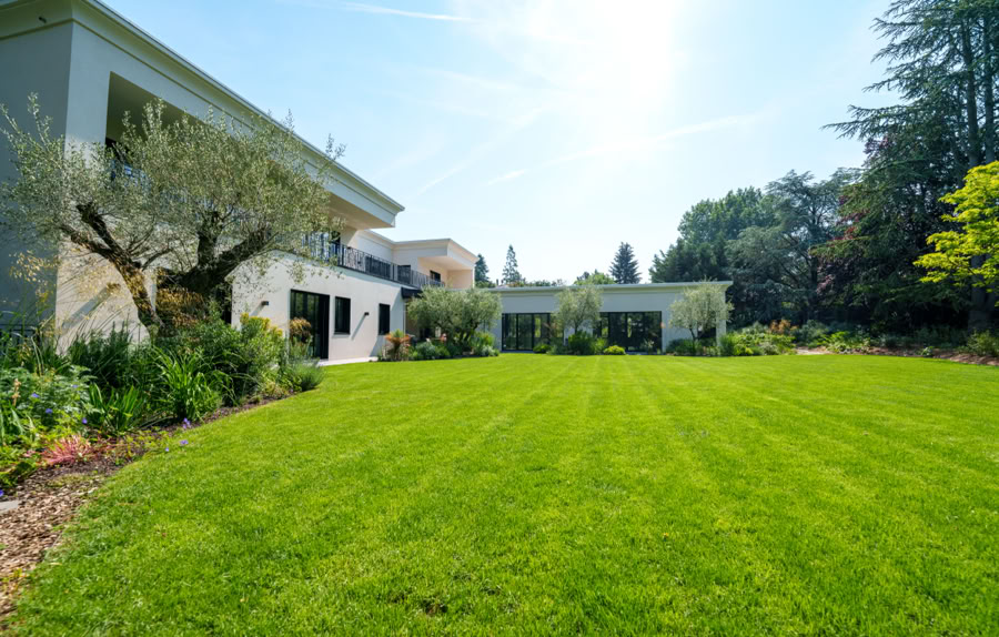 Grande pelouse verte devant une maison moderne avec des arbres et un ciel bleu à Collonge-Bellerive.