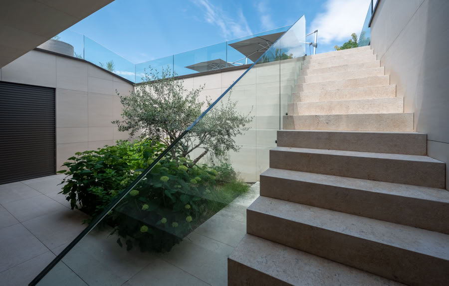 Escalier en pierre avec balustrade en verre, plante verte à gauche, ciel bleu en arrière-plan à Cologny.