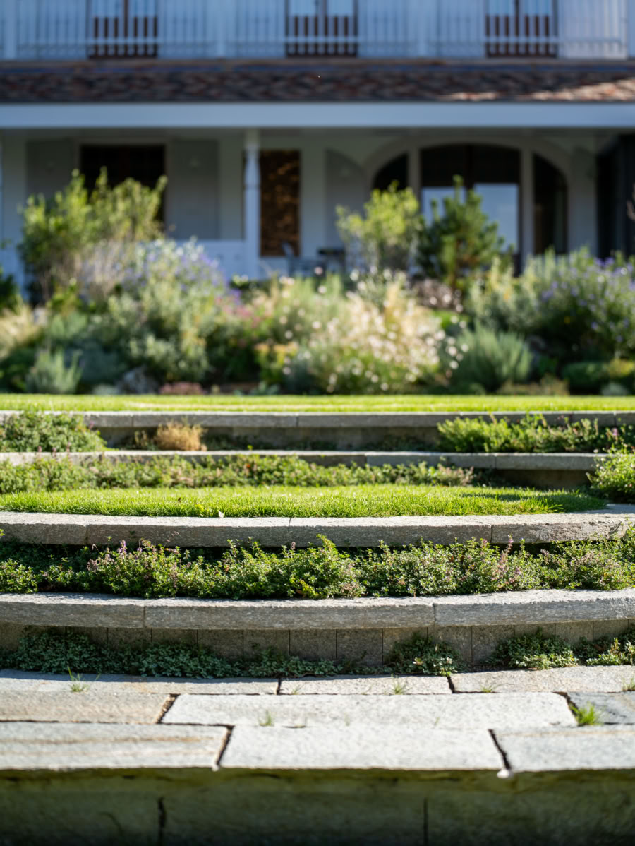Jardin à Collonge-Bellerive en terrasses avec des plantes vertes devant une maison à deux étages avec balcons et fenêtres.