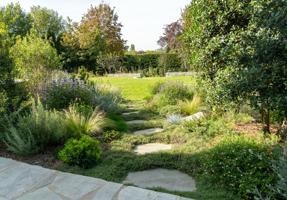 Jardin à Collonge-Bellerive avec pelouse, arbres, arbustes et chemin en pierre.