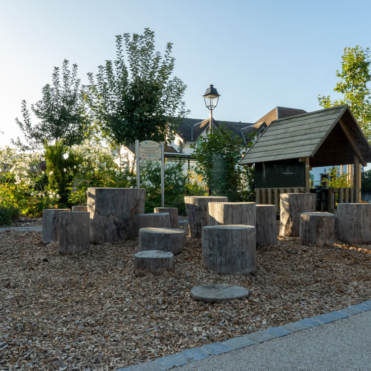 Aire de jeux extérieure avec des structures en bois, entourée de végétation et d'un bâtiment en arrière-plan.