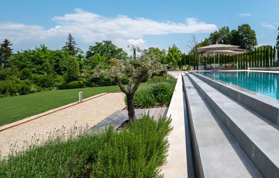Piscine extérieure avec des marches en pierre, entourée de verdure et d'arbres sous un ciel bleu à Cologny.