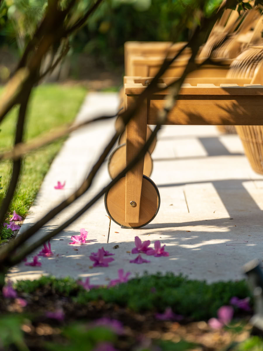 Banc en bois sur une terrasse avec des pétales de fleurs roses éparpillés au sol, entouré de verdure.