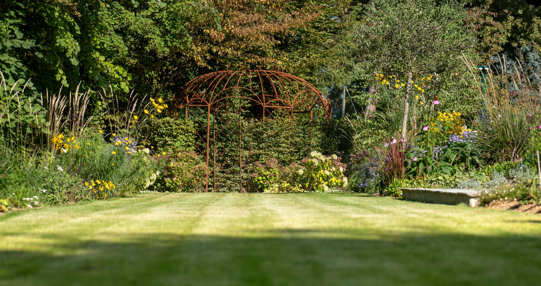 Pelouse verte entourée de buissons et d'arbres avec des fleurs jaunes et rouges à Collonge-Bellerive.