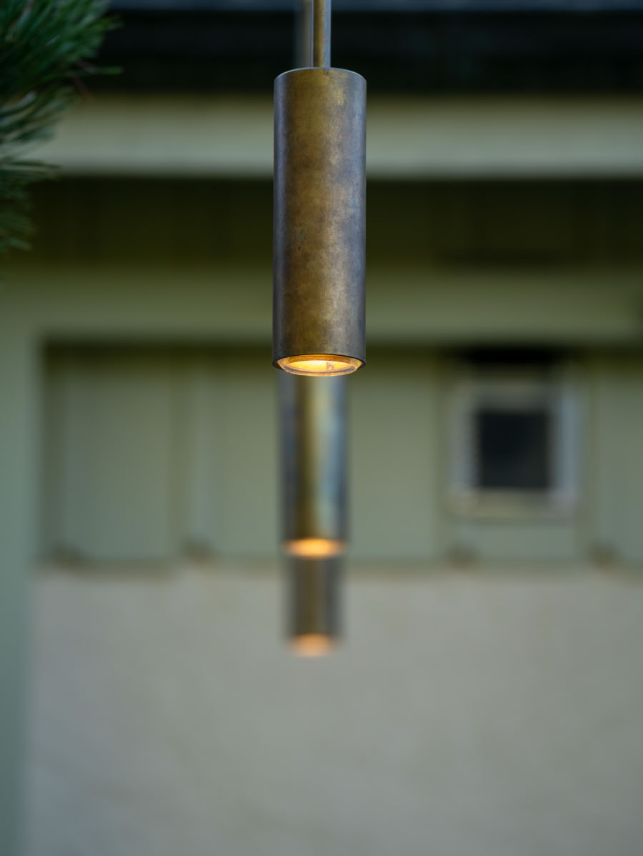 Lampe suspendue cylindrique en métal avec un fond flou montrant un mur et une fenêtre.