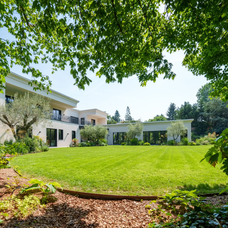 Grande maison blanche avec un jardin verdoyant, entourée d'arbres et de buissons à Collonge-Bellerive.