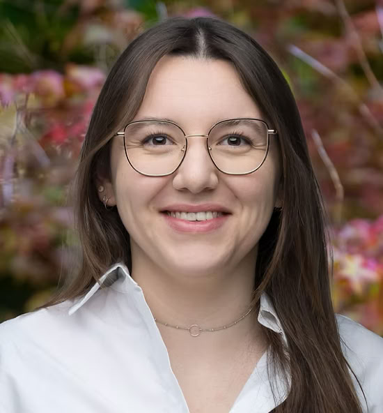 Elyne Barbey souriant portant une chemise blanche, avec un fond flou de feuillage coloré.