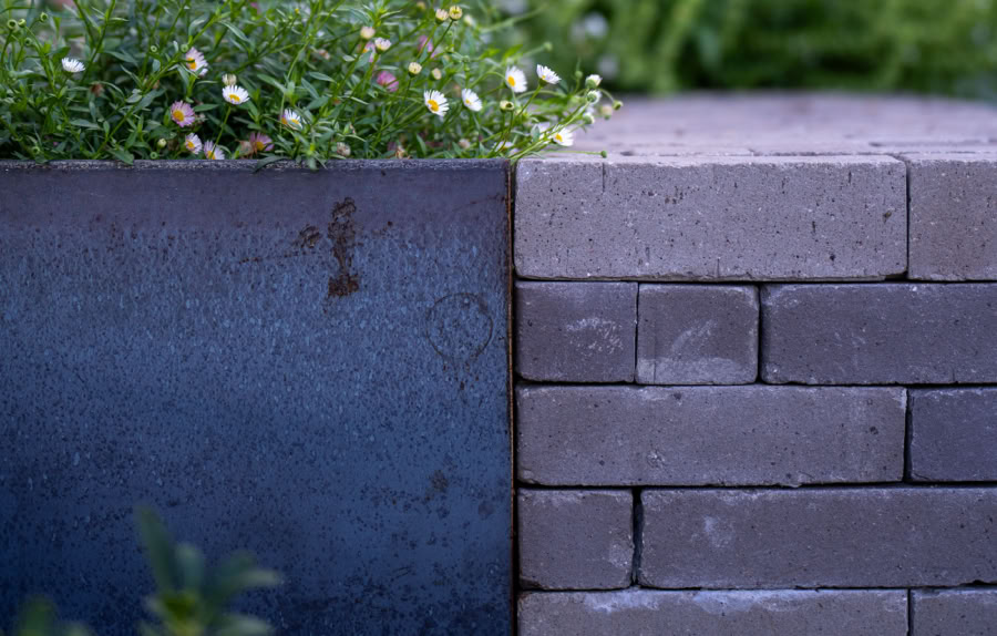 Mur en briques avec des plantes vertes et fleurs blanches en arrière-plan flou.