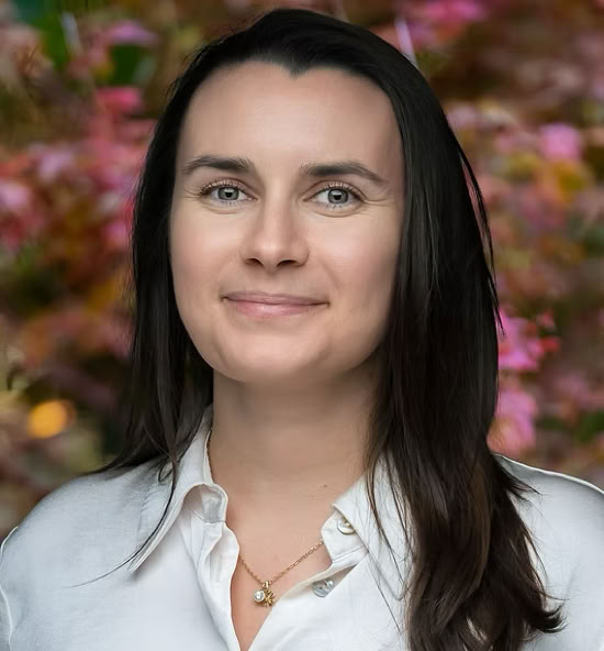 Mathilde Pochintesta souriant portant une chemise blanche, avec un fond flou de feuillage coloré.