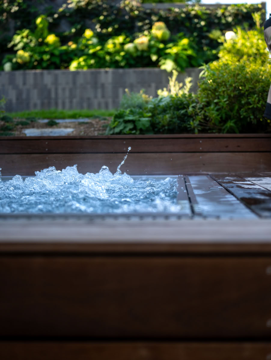 SPA avec de l'eau bouillonnante, entouré de bois, avec des plantes vertes en arrière-plan à Meinier.
