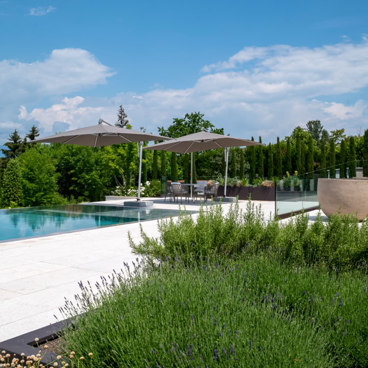 Piscine extérieure entourée de végétation, avec des parasols et des chaises longues, sous un ciel bleu partiellement nuageux.