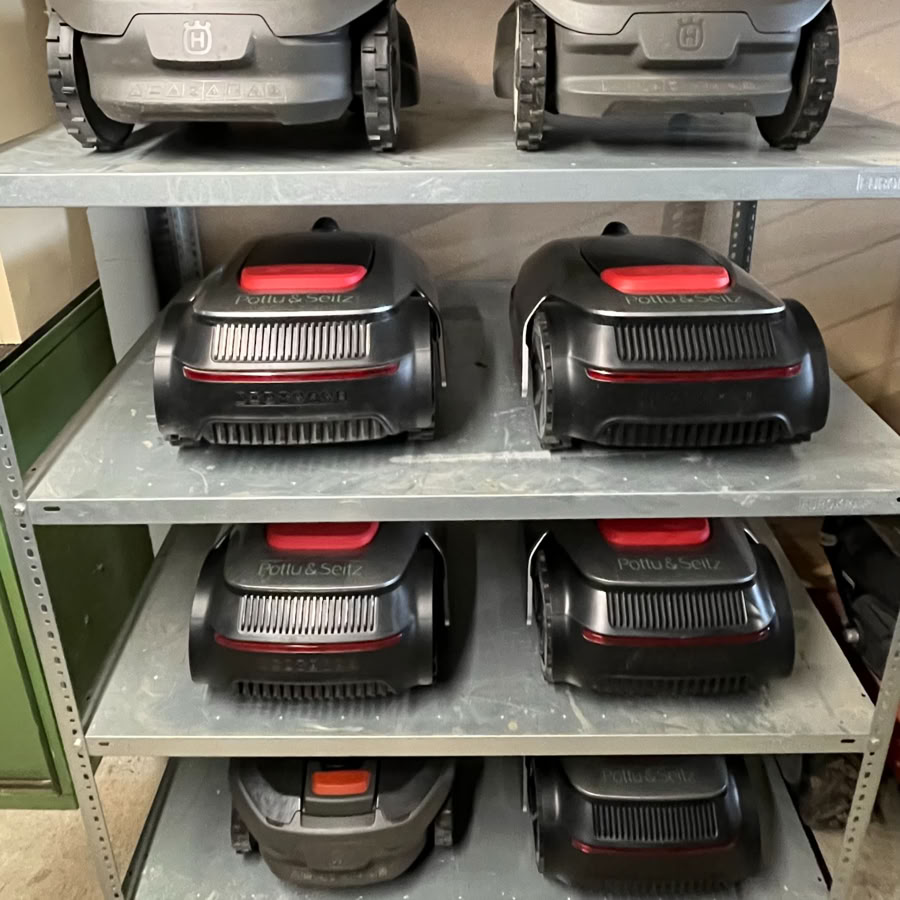 Plusieurs tondeuses robotisées Dreame noires et grises sur des étagères métalliques en hivernage.