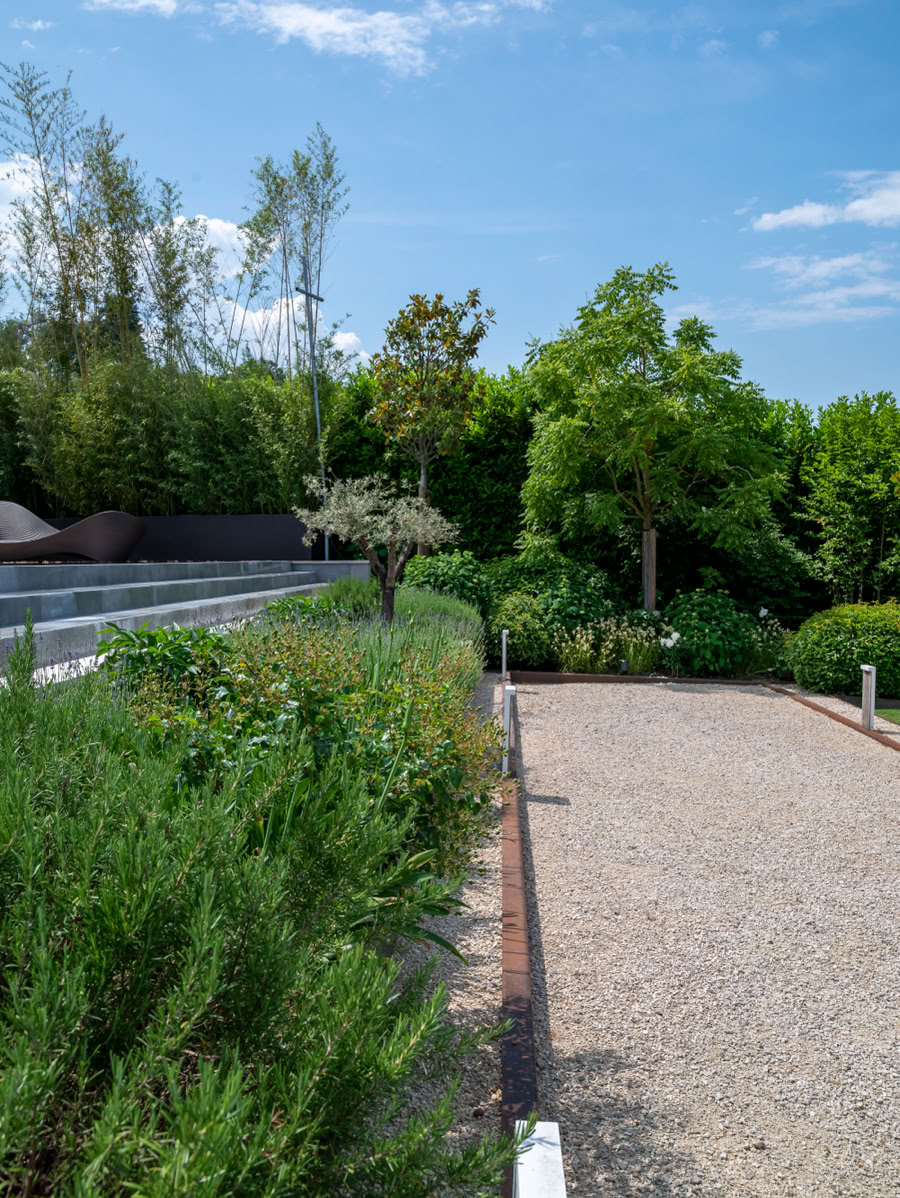 Terrain de pétanque bordée de plantes vertes et d'arbres sous un ciel bleu à Cologny.