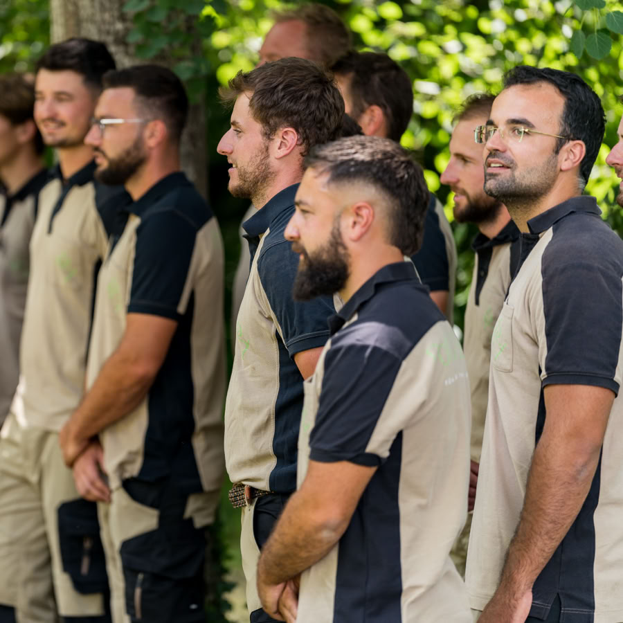 Un groupe d'employés Pottu & Seitz en uniforme beige et noir, debout en extérieur devant des arbres.