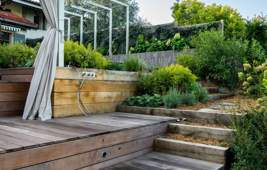 Escalier en bois menant à une terrasse avec des plantes vertes et des structures métalliques, ciel bleu en arrière-plan à Meinier.