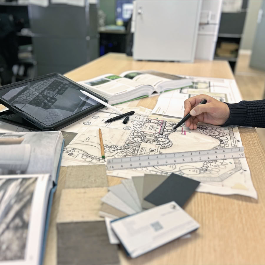 Architecte paysagiste genève et vaud dessinant sur un plan architectural avec des échantillons de couleurs et une tablette sur la table.